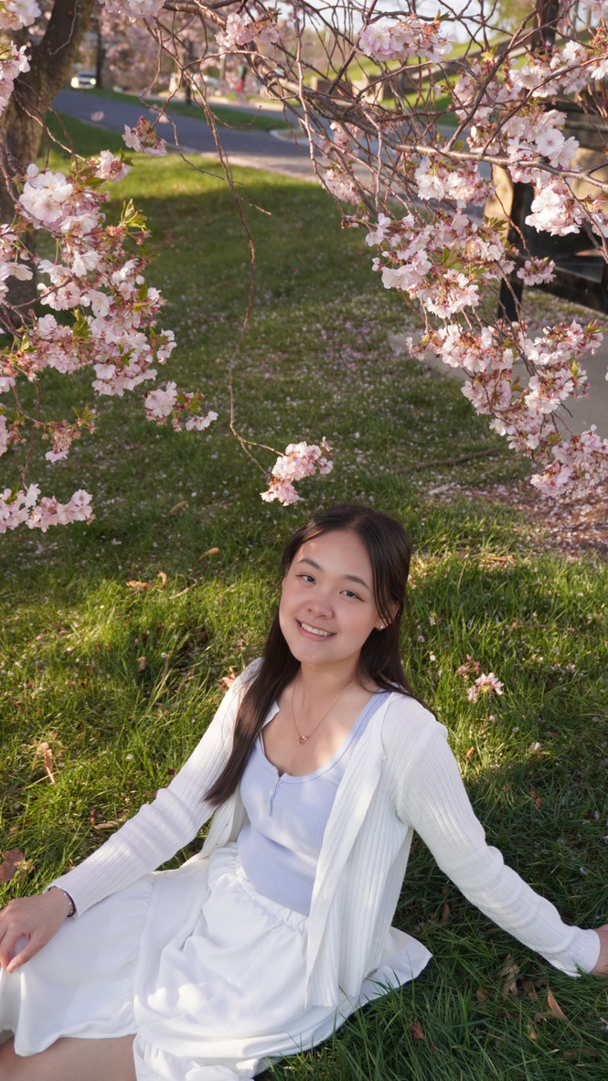Xintong sitting outside under a tree with cherry blossoms